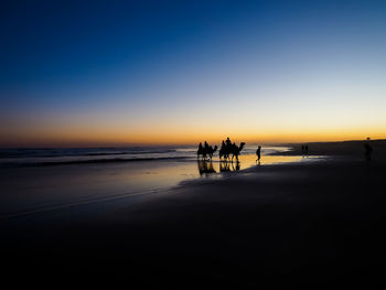 Silhouette people on beach against clear sky during sunset