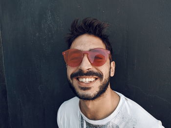 Portrait of smiling young man wearing sunglasses standing against wall