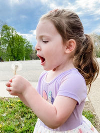 Close-up of girl looking away blowing on a dandelion