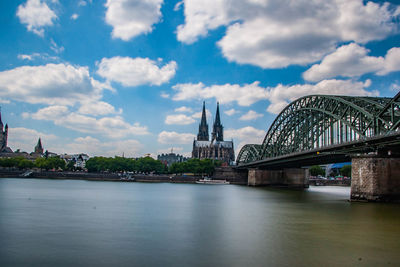 Arch bridge over river by buildings against sky