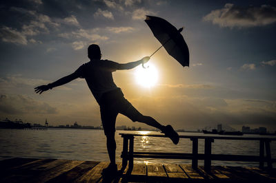 Rear view of man standing with umbrella against lake during sunset