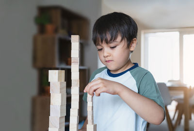 Cute boy stacking block shape on table at home