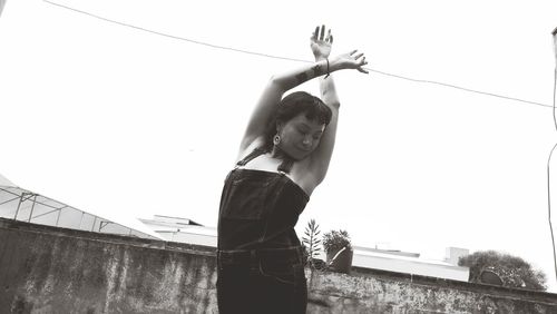 Low angle view of woman with arms raised standing against clear sky