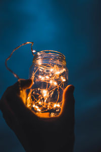 Close-up of hand holding jar with illuminated string lights at night