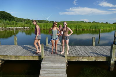 People sitting on pier over lake against sky