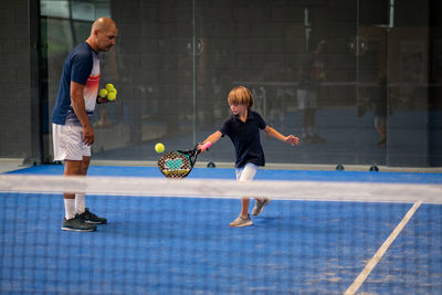 Monitor teaching padel class to child, his student - trainer teaches little boy how to play padel 