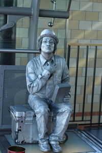 Portrait of mime painted in silver sitting on box against wall