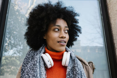 Afro woman with headphones contemplating against glass wall