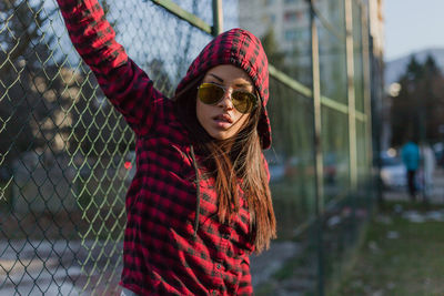 Close-up portrait of woman in sunglasses standing against fence