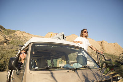 Young couple in mini van enjoying vacation against clear blue sky