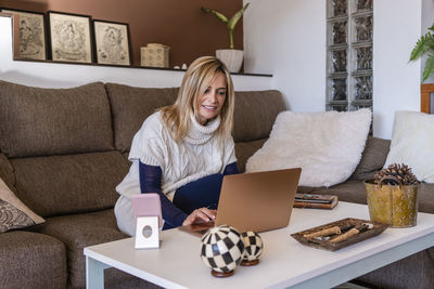 Young woman using phone while sitting on sofa at home