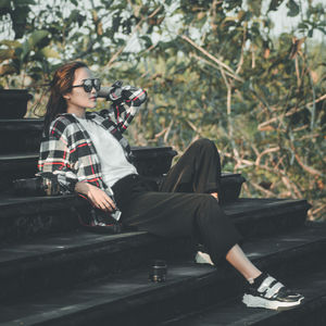 Side view of woman photographing while sitting on tree