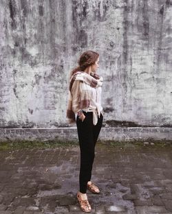Full length of young woman looking away while standing against wall