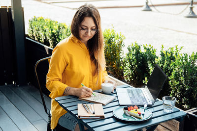 Mental health mood tracker, woman sitting in street cafe and fills mood tracker in notepad