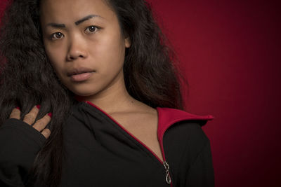 Portrait of young woman wearing jacket against red background