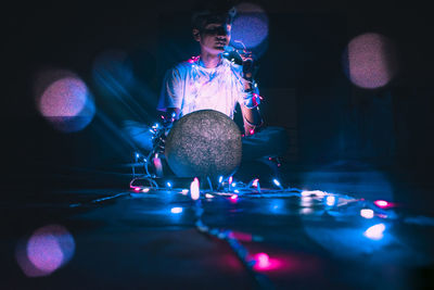 Full length of man sitting on floor with illuminated string light