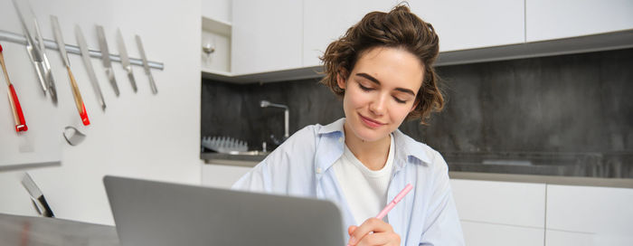 Young woman using laptop while standing in office