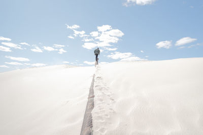 Man walking on snow covered land against sky