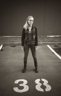 Portrait of young woman standing by number 88 at parking lot
