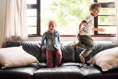 Cute sibling jumping on sofa at home