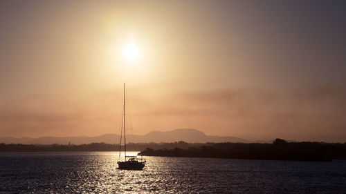 Silhouette sailboat sailing on sea against sky during sunset