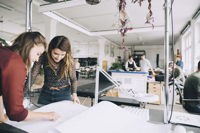 Female entrepreneurs discussing over paper at table in creative office