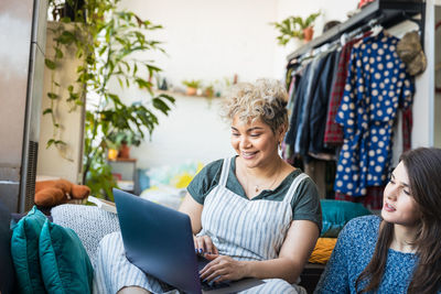 Friend looking at woman using laptop while sitting in living room at home