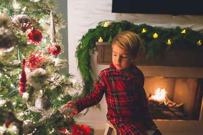 Boy hanging ornaments on christmas tree at night time