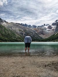 Rear view of man standing in lake against mountain