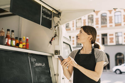 Female chef using mobile phone while looking at menu on food truck