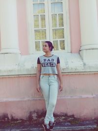 Portrait of young woman standing against wall