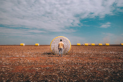 Rear view of man standing by hay bale on land against sky