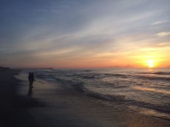 Silhouette people standing on beach against sky during sunset