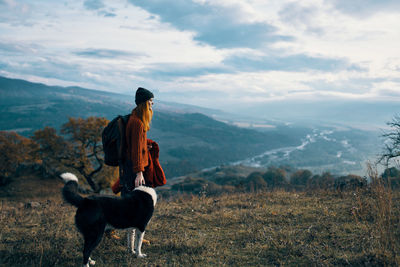 Man with dog standing on mountain against sky