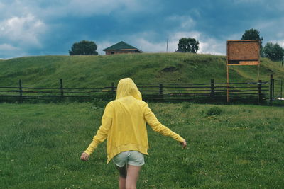 Rear view of woman walking on grassy field against cloudy sky