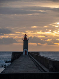 Lighthouse by sea against sky during sunset