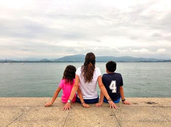 Rear view of women and children sitting on sea against sky