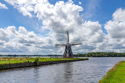 Traditional windmill on field by river against sky