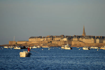 Sailboats in sea by buildings against clear sky