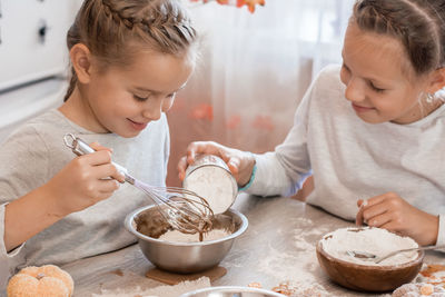 Preparing to celebrate halloween and preparing a treat. two girls add wheat flour to baking cookie 