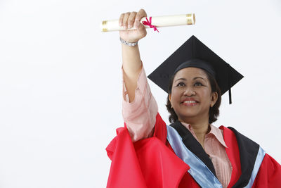 Portrait of woman in graduation gown against white background