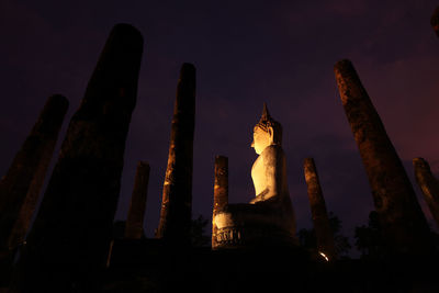 Low angle view of buddha statue and temple against sky at night