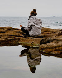 Rear view of woman sitting on beach meditating 