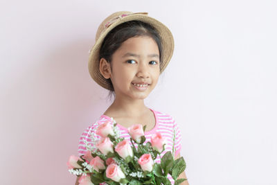 Portrait of smiling girl holding flower against white background