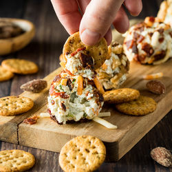 A hand dipping a cracker into a dill pickle cream cheese fat bomb.