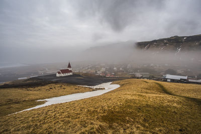 Scenic view of land by buildings against sky during winter