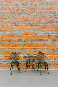 Empty chairs and table against brick wall