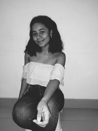 Portrait of smiling young woman sitting against wall at home