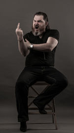 Mid adult man gesturing obscene gesture while sitting against black background