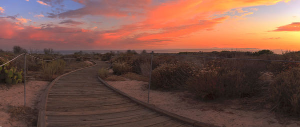 Scenic view of boardwalk against sky during sunset